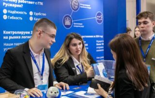 Trzy osoby przy stoisku targowym z materiałami informacyjnymi na stole